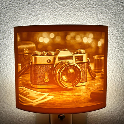 Warm glowing camera lithophane night light featuring a detailed vintage-style camera on a tabletop with blurred background lights, curved photography-themed decor for bedrooms, offices, studios, or camera lovers.