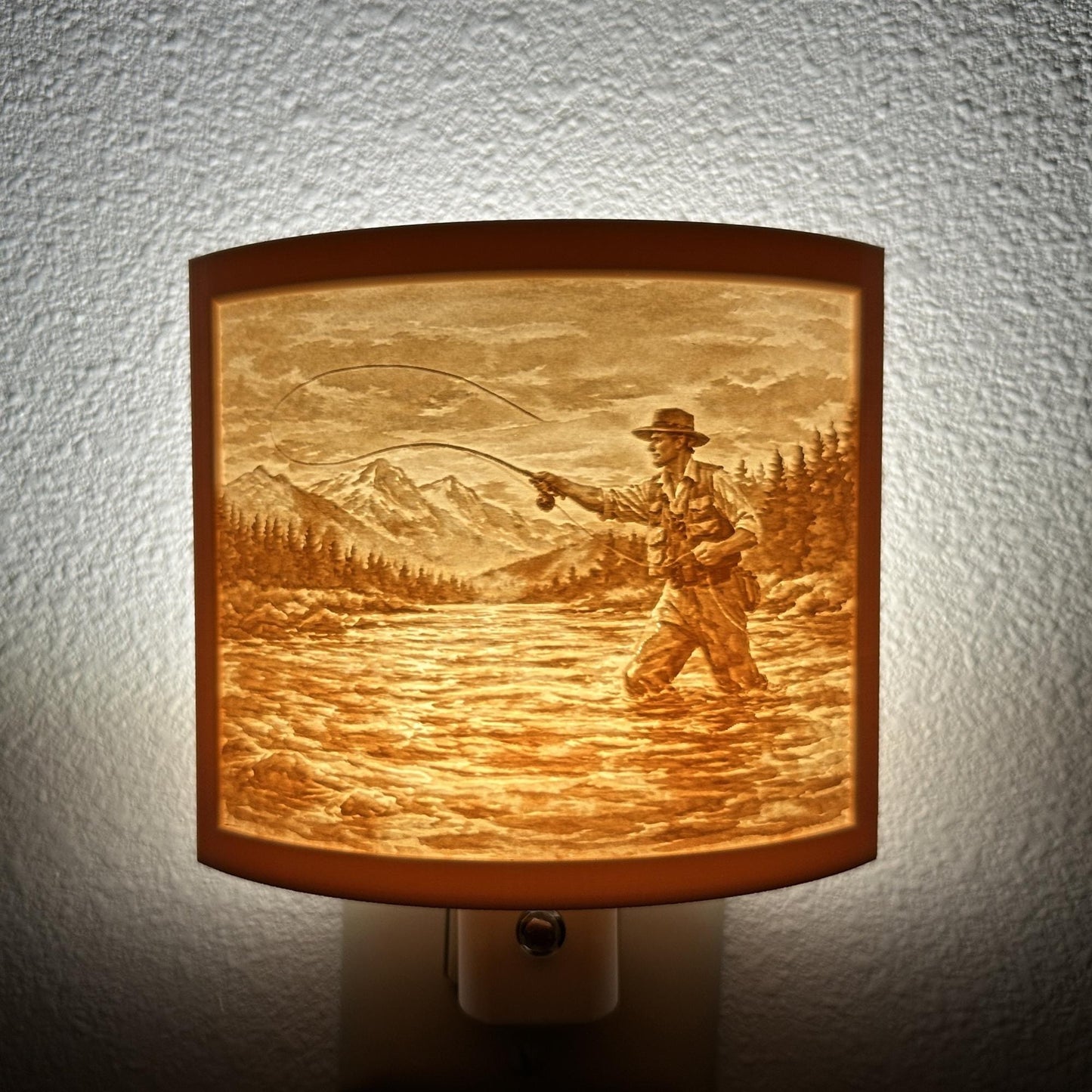 Warm glowing fishing lithophane night light featuring a fly fisherman casting in a mountain river with forest and mountain scenery, curved outdoor-themed decor for cabins, lodges, fishing enthusiasts, or rustic spaces.