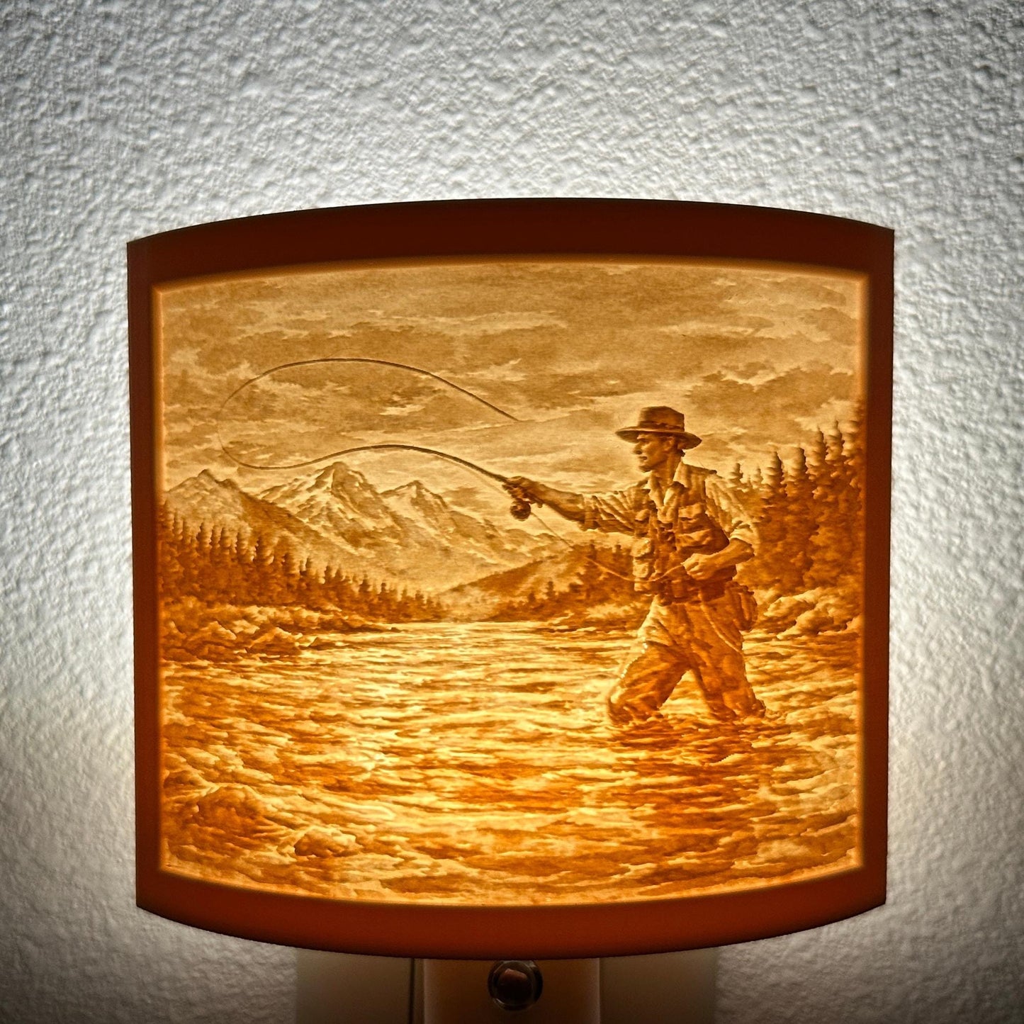 Warm glowing fishing lithophane night light featuring a fly fisherman casting in a mountain river with forest and mountain scenery, curved outdoor-themed decor for cabins, lodges, fishing enthusiasts, or rustic spaces.