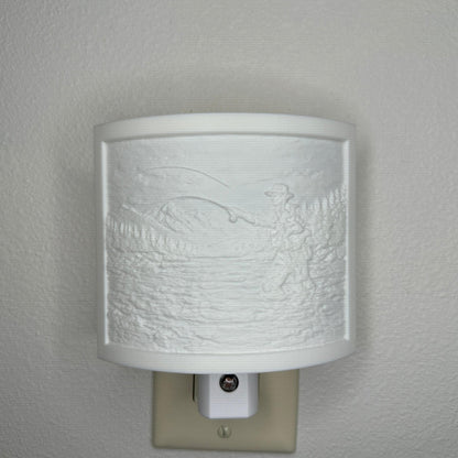 White fishing lithophane night light with embossed fly fisherman casting in a mountain river surrounded by forest and mountain scenery, curved outdoor-themed decor for cabins, lodges, fishing enthusiasts, or rustic spaces.